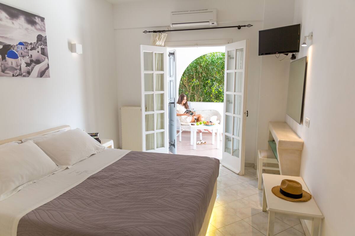 Une chambre avec un lit, une télévision, un bureau et une vue sur une terrasse extérieure.