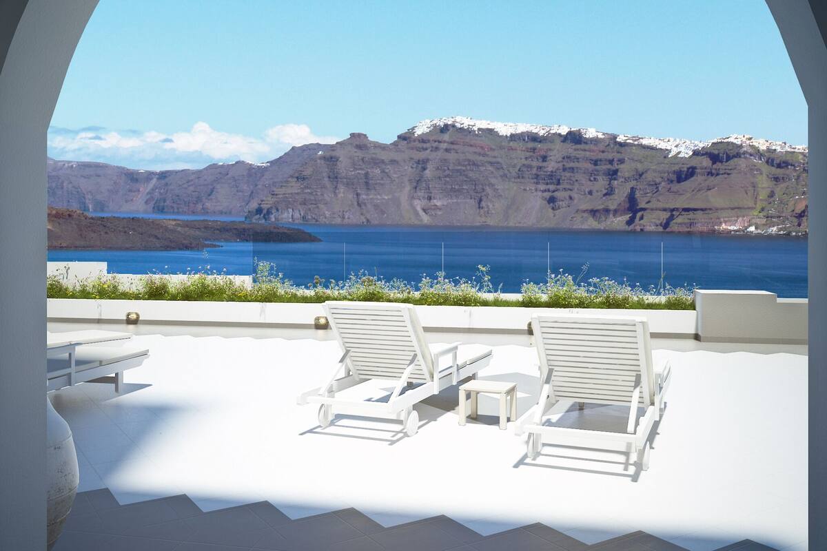 Une terrasse dotée de chaises longues blanches et offrant une vue sur un paysage côtier, avec des falaises et une étendue d’eau.
