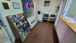 Una pequeña recepción con un reloj, un letrero de neón, un tablón de anuncios y una ventana con persianas.