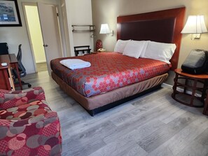 A hotel room with a bed, a chair, a desk, a lamp, and a door.