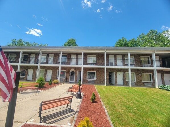 Two-story motel with a brick facade and a flat roof, featuring windows on each floor and a small front garden with a bench.
