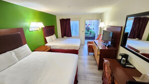 Habitación de hotel con dos camas, un escritorio con televisor, una silla y un ventanal con cortinas.