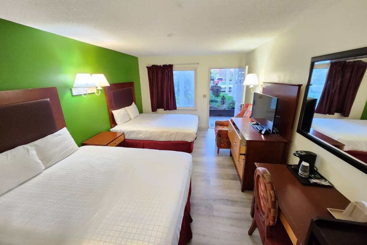 Quarto de hotel com duas camas, uma mesa de trabalho com televisão, uma cadeira e uma janela com cortinas.