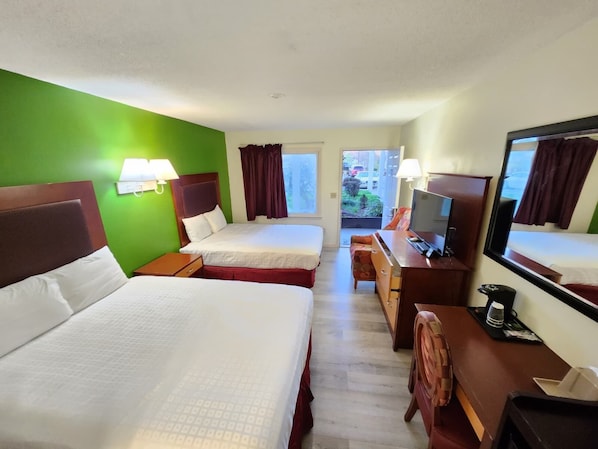 A hotel room with two beds, a desk with a TV, a chair, and a window with curtains.