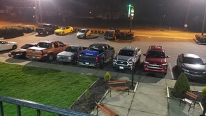 Un estacionamiento con varios vehículos, incluyendo camiones y automóviles, y una luz de semáforo verde.