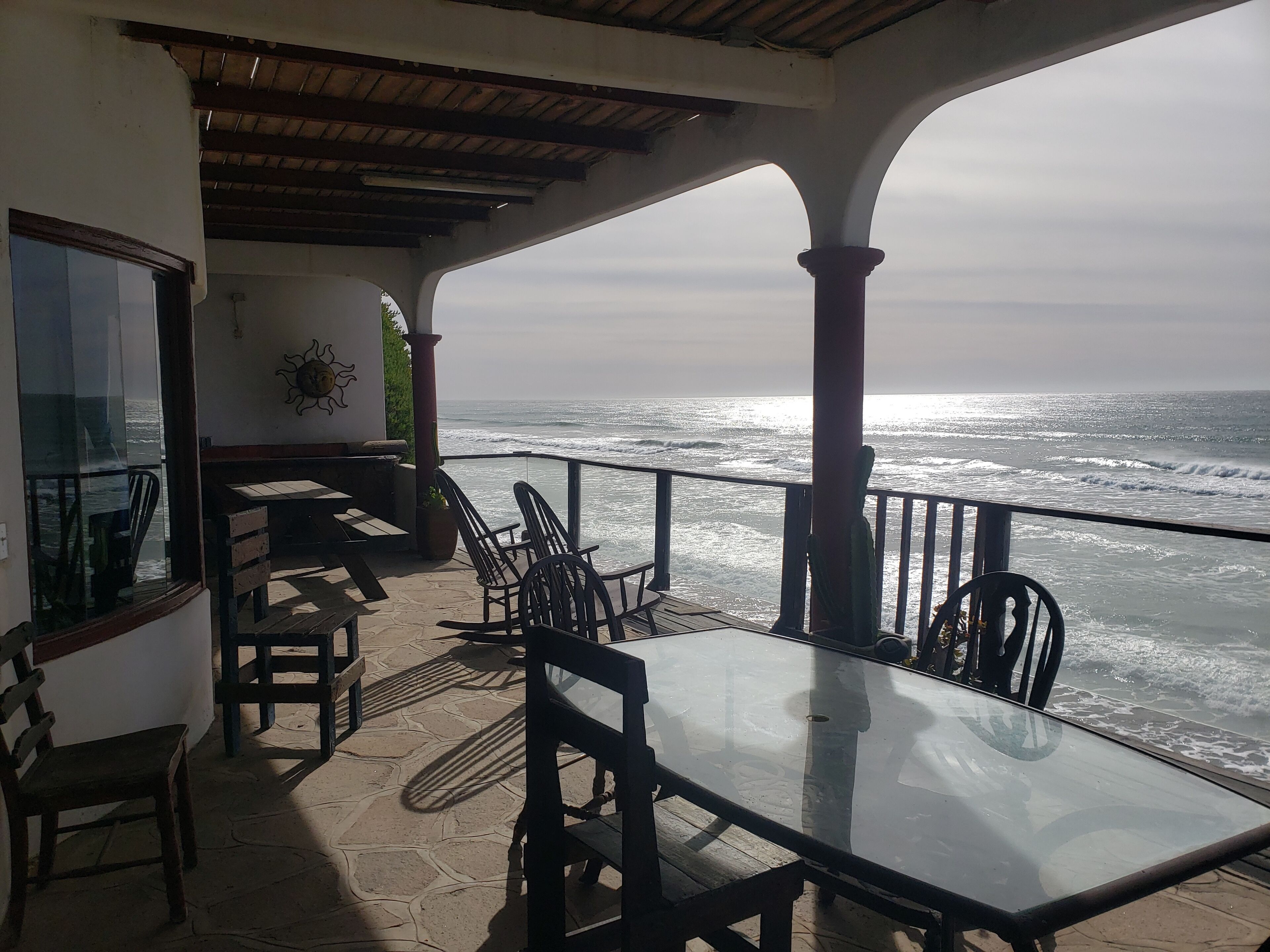 A covered outdoor seating area with a table and chairs, overlooking the ocean.