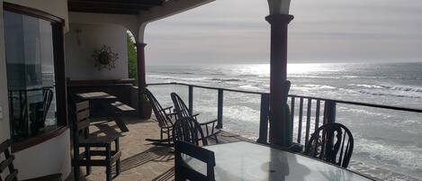 A covered outdoor seating area with a table and chairs, overlooking the ocean.