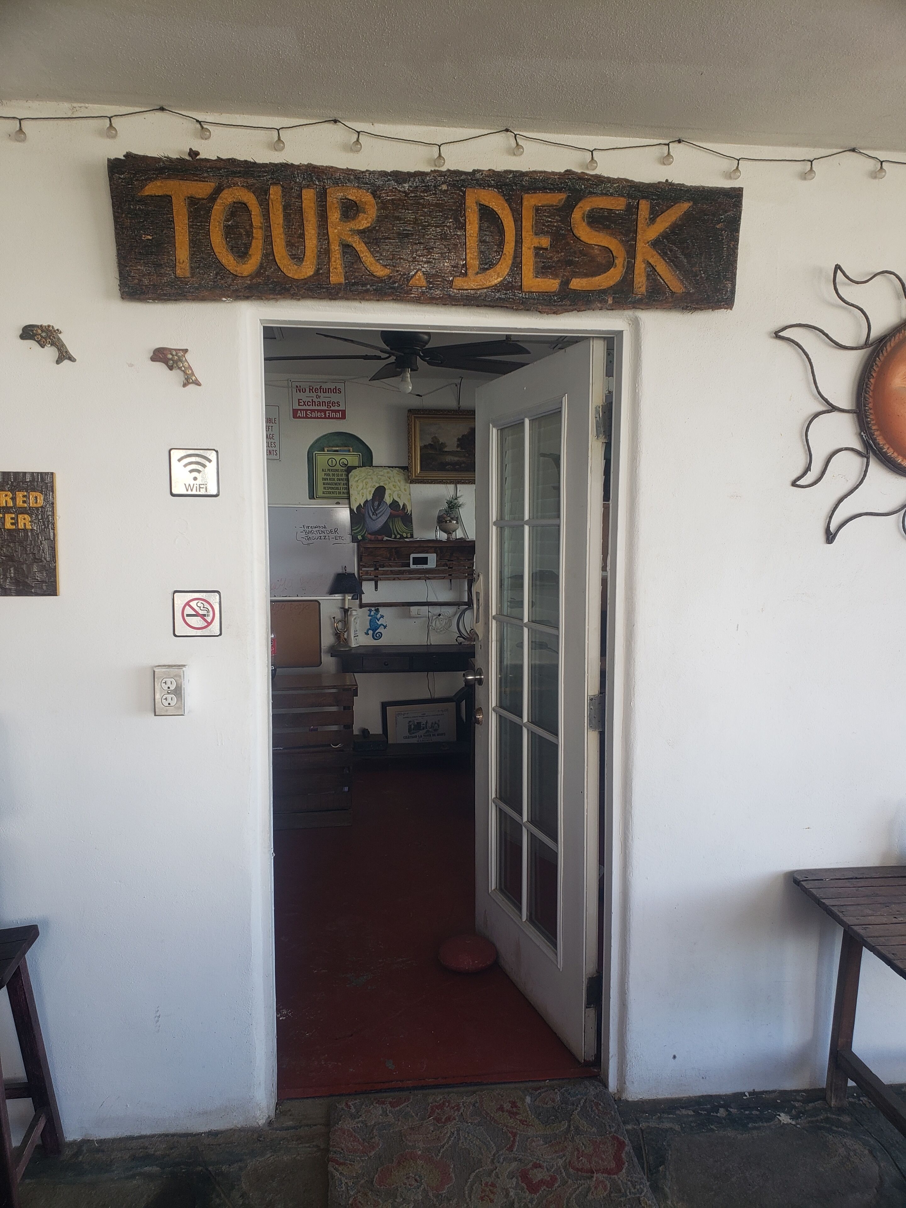 Una habitación con un cartel de 'TOUR DESK', un cartel de 'No se aceptan devoluciones ni cambios. Todas las ventas son definitivas', un cartel de 'WiFi', un cartel de 'No fumar' y un cartel de 'Tierra Roja'.