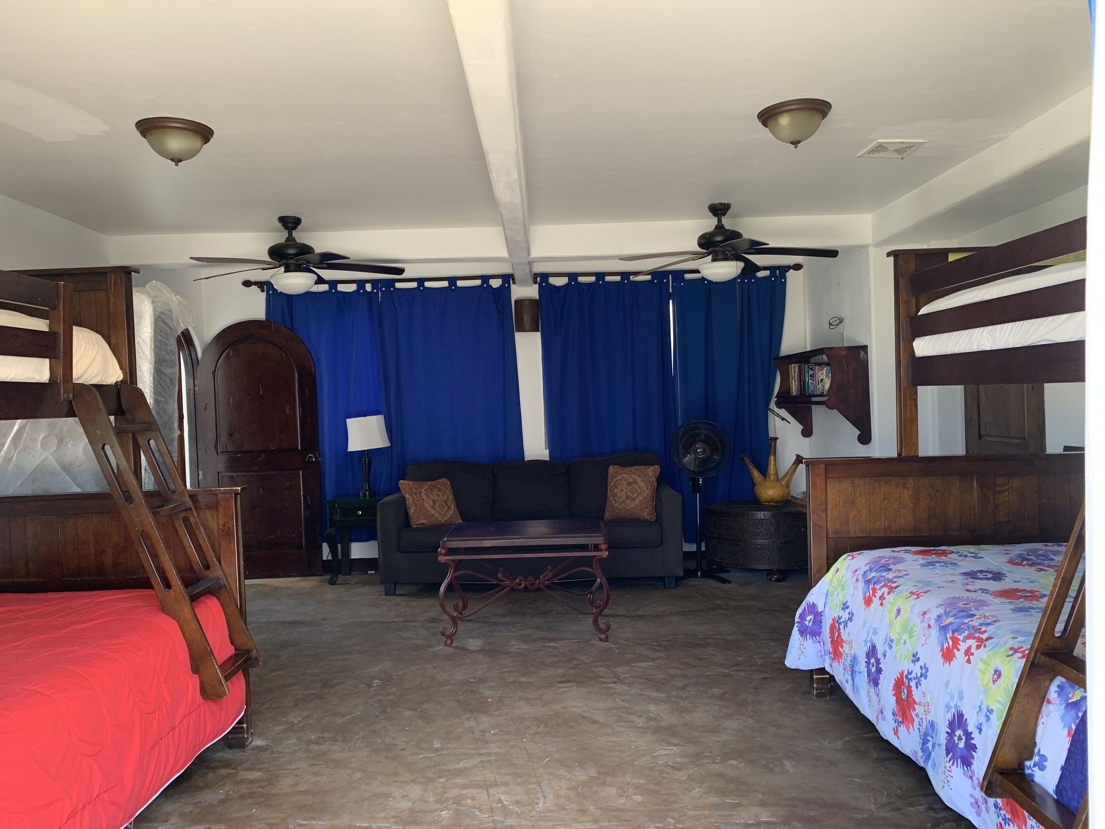 A room with bunk beds, a sofa, a table, and ceiling fans.