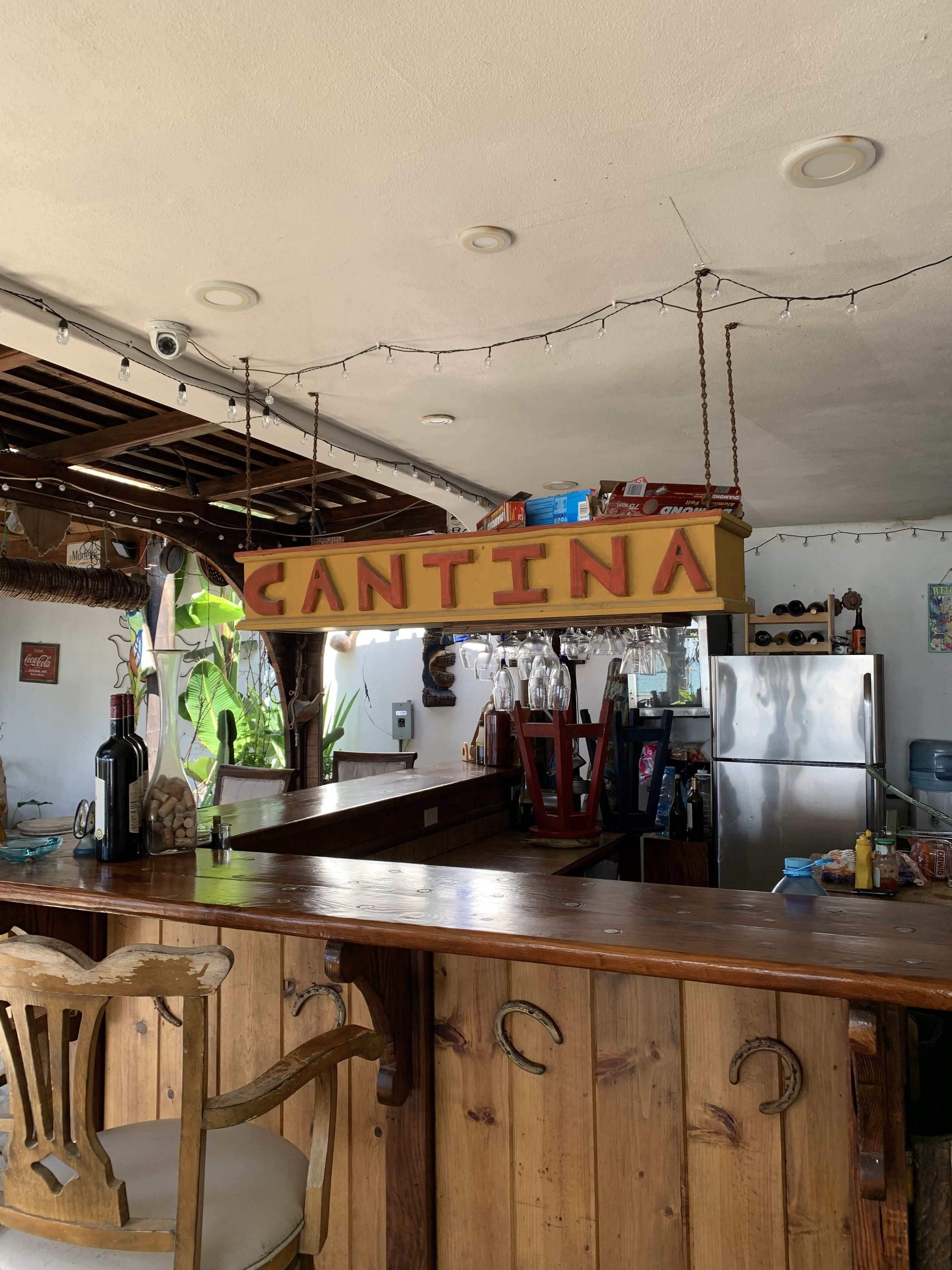 Une cuisine rustique avec un comptoir-bar en bois, un réfrigérateur en acier inoxydable et une enseigne suspendue sur laquelle on peut lire « CANTINA ».