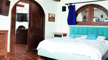A bedroom with a wooden wardrobe, a bed with patterned bedding, a wooden headboard, and a large arched mirror.