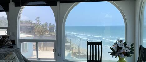 A room with a large window offering a view of the ocean, a ceiling fan, and a chair by the window.