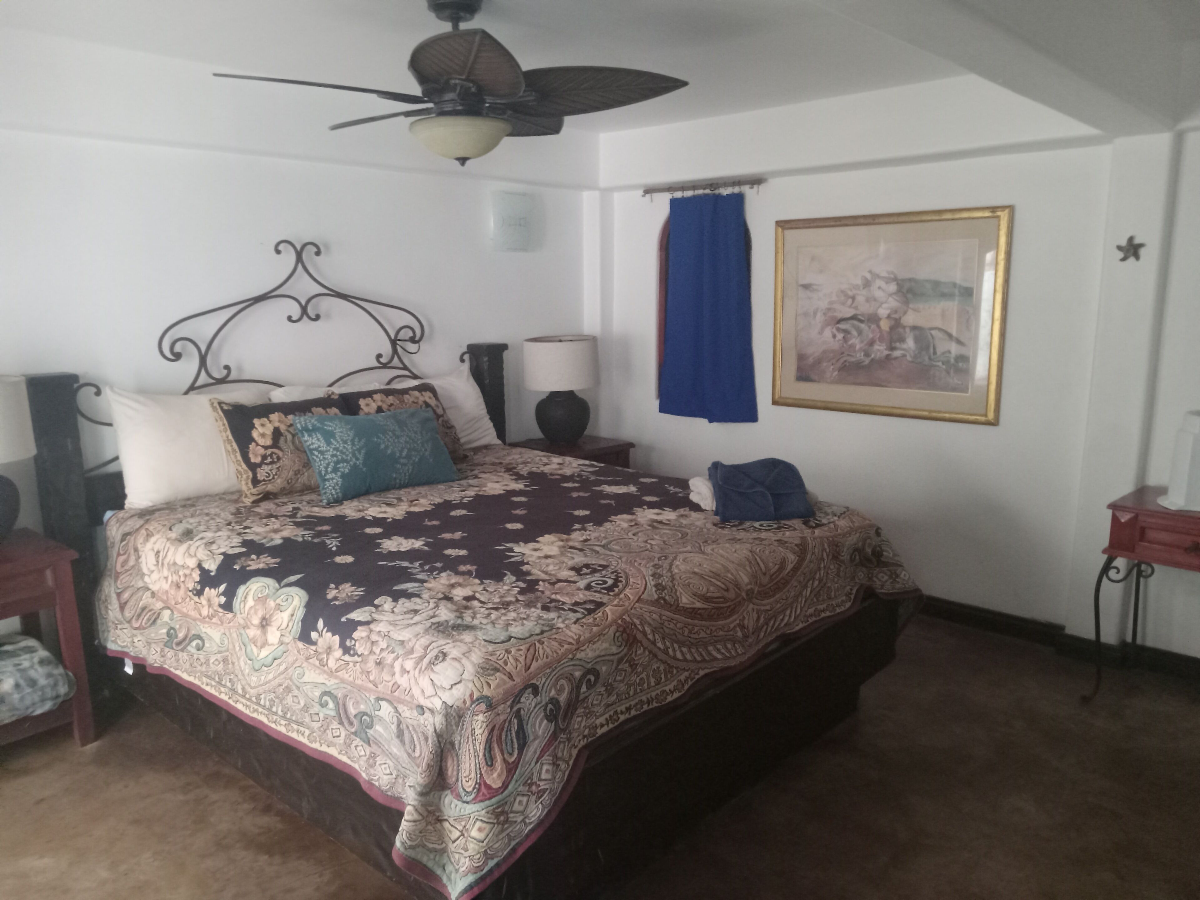 Un dormitorio con una cama grande, un ventilador de techo, una mesita de noche, una lámpara, un cuadro enmarcado y una decoración de estrella en la pared.