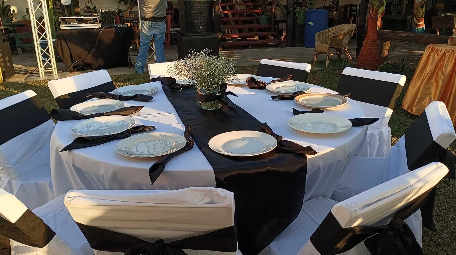 Mesa redonda dispuesta para una comida, con manteles blancos y fundas negras para las sillas.