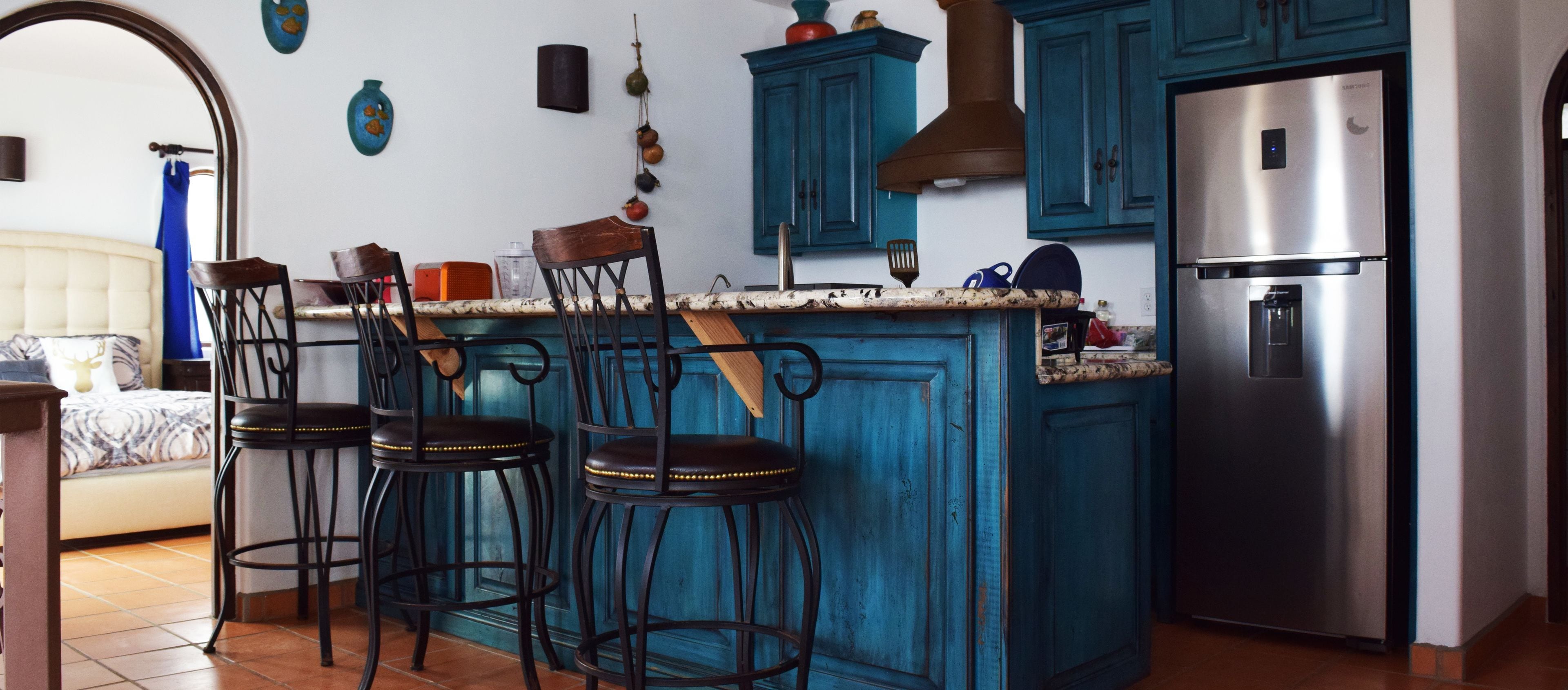 A kitchen with teal cabinets, a stainless steel refrigerator, and three bar stools.