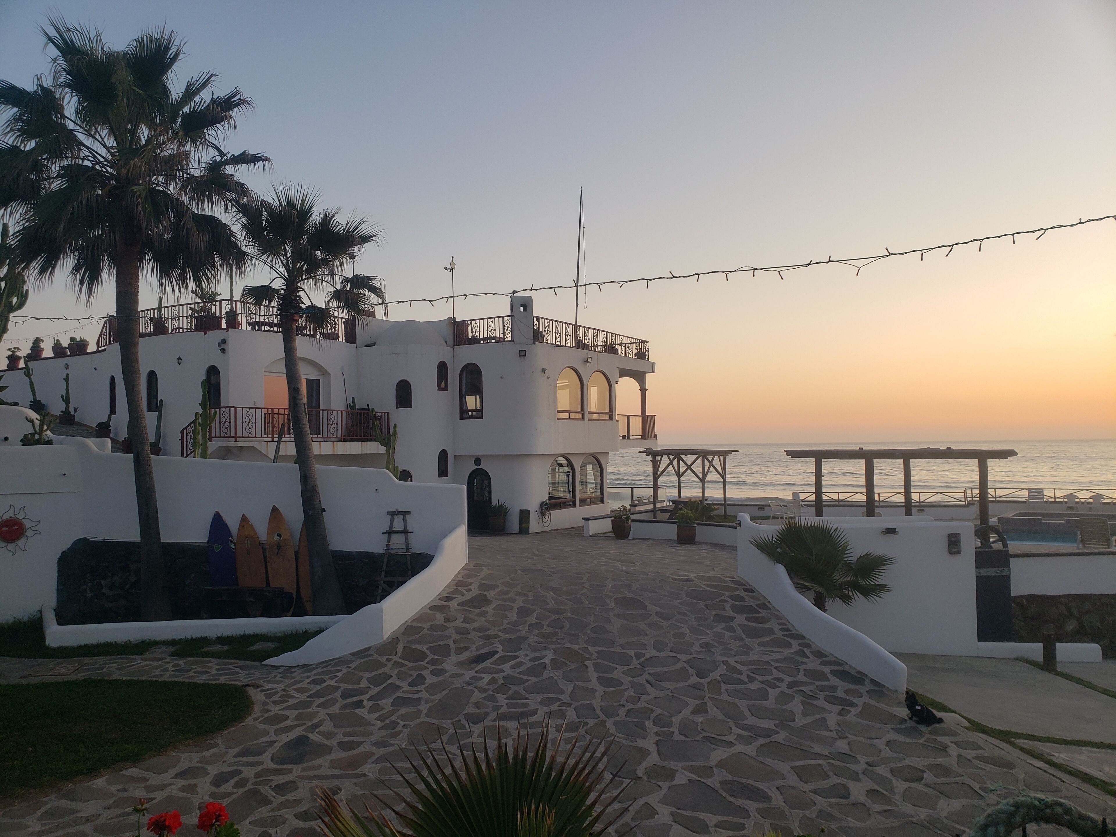 A white building with a stone pathway leading to a pool area, overlooking the sea.