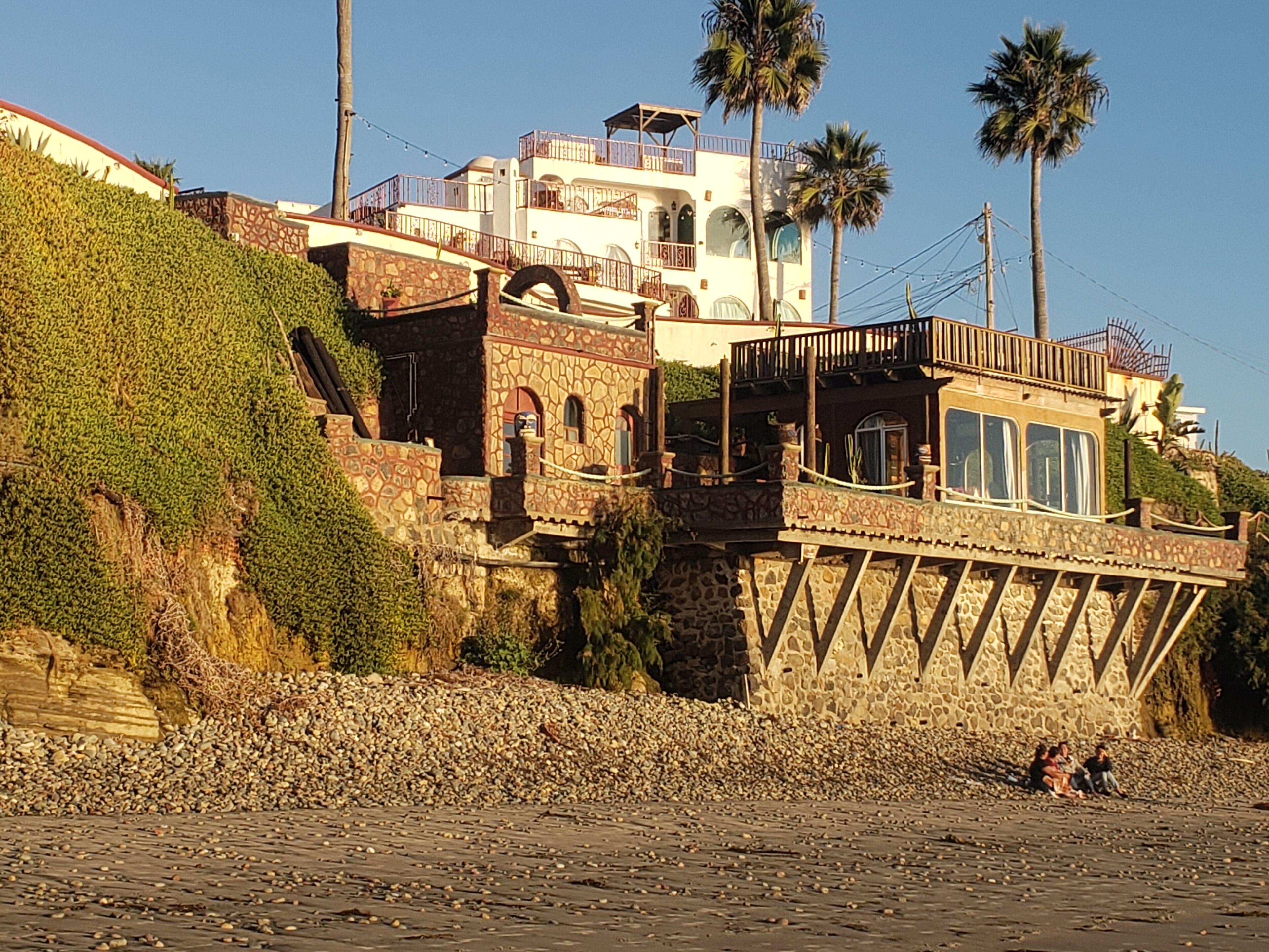 Un bâtiment situé sur la côte, doté d’une façade en pierre, de nombreux balcons et offrant une vue sur la plage.