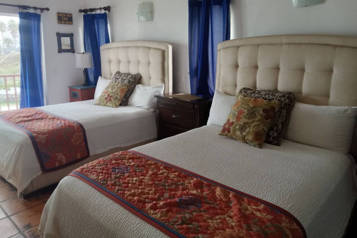 Een hotelkamer met twee bedden, elk met een kussen met bloemenprint, een rood-beige sprei en een nachtkastje ertussen.