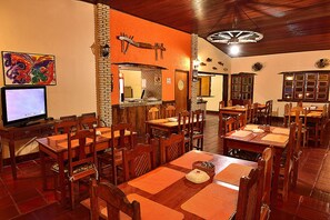 A restaurant with wooden tables and chairs, a television, and a brick wall. - Pousada Piuval (Pocone)