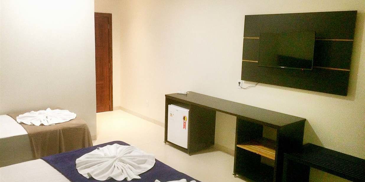 A hotel room with a bed, a small table with a white cloth, a TV mounted on the wall, and a minibar.