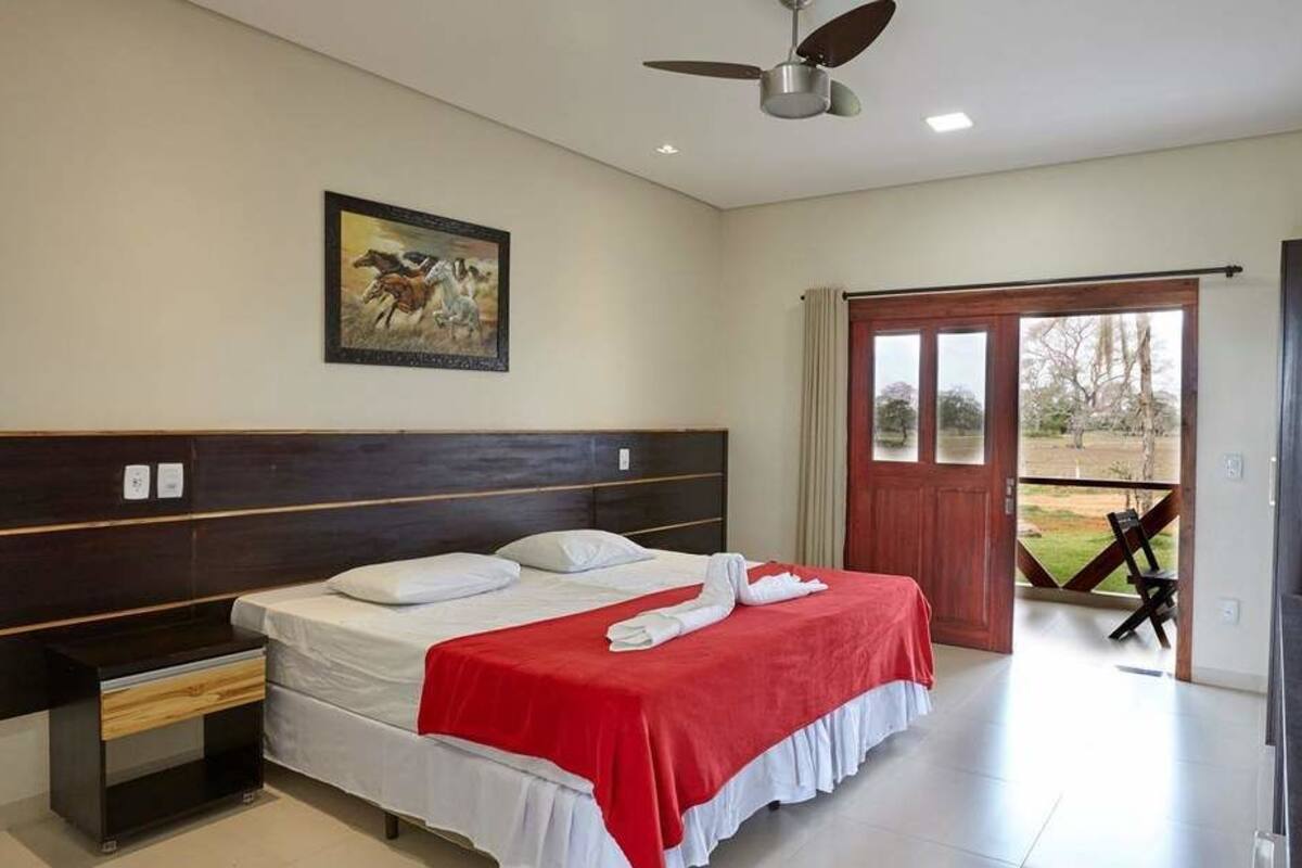A bedroom with a bed, a nightstand, a ceiling fan, a painting, and a sliding door leading to a balcony.