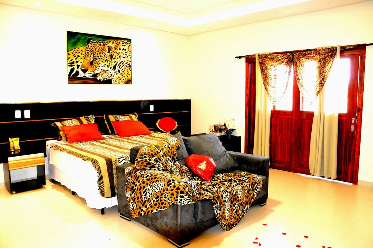 A bedroom with a large bed, a sofa, a painting of a leopard, and a window with curtains.