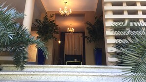 A hotel lobby with a chandelier, large potted plants, and a staircase leading to an upper level. - Palm Residence (Petionville)