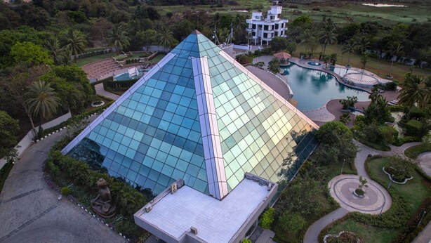 A modern building with a glass facade, surrounded by landscaped gardens and a swimming pool. - Eskay Resorts (Mumbai)