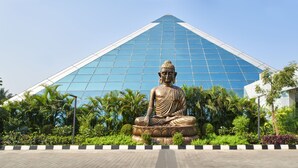 A large Buddha statue in front of a modern glass building. - Eskay Resorts (Mumbai)