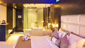 A modern hotel room with a large bed, a bathroom with a glass enclosure, and a seating area with a coffee machine. - Eskay Resorts (Mumbai)