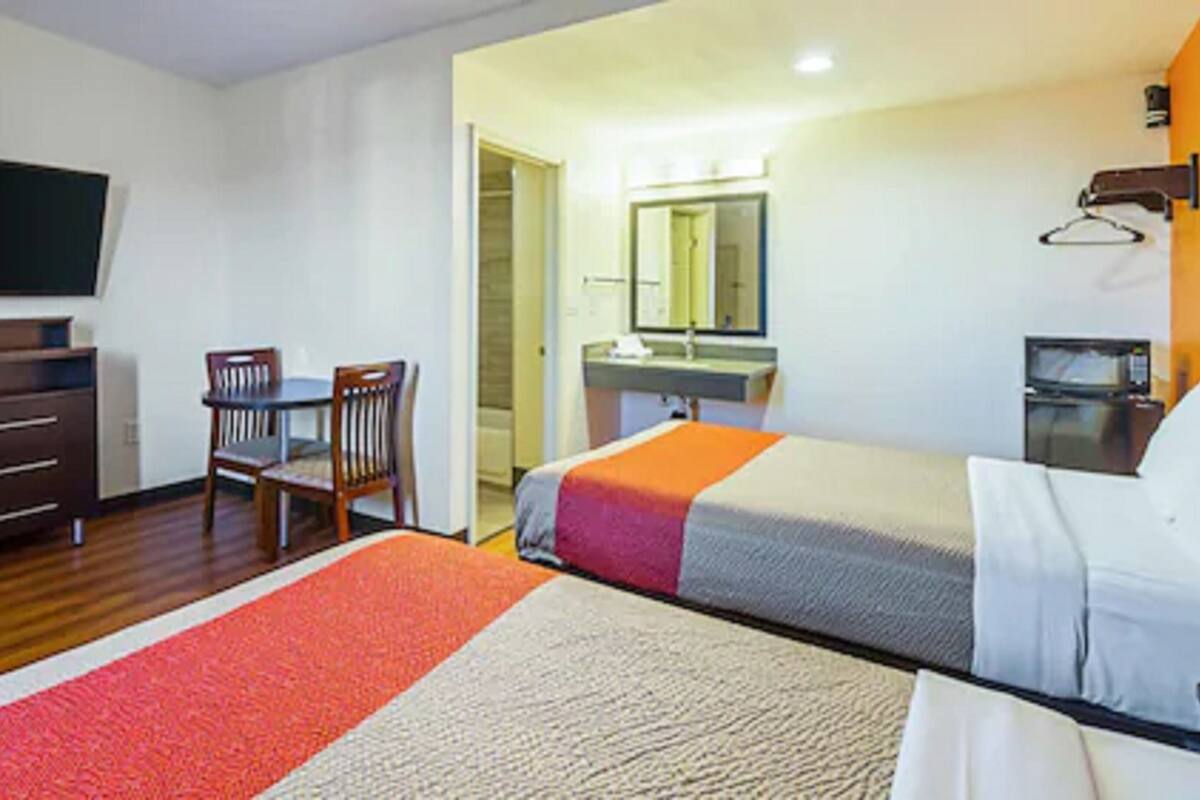 A hotel room with a bed, a desk, a chair, a television, a mirror, and a microwave.