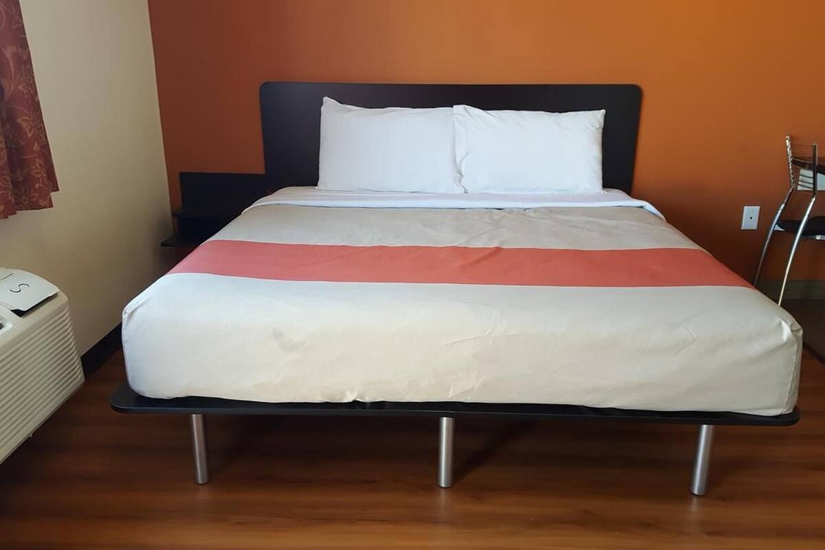 A bed with a white and red bedspread, a black headboard, and a white pillow.