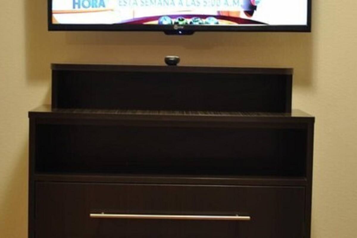 A television mounted on a wall above a dark wooden cabinet with a drawer.