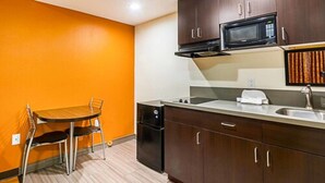 A compact kitchen with a microwave, sink, and a dining area with a table and chairs. - Motel 6 on Maple (Hesperia)