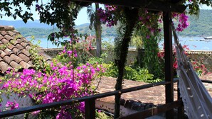 Vista desde un área exterior cubierta con una pérgola, vibrantes flores de buganvilla rosadas y un paisaje con un lago y montañas.