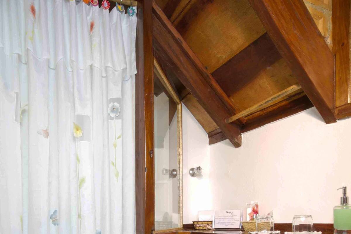 A bathroom with a toilet, a shower curtain, a wooden ceiling, and a sink with toiletries.