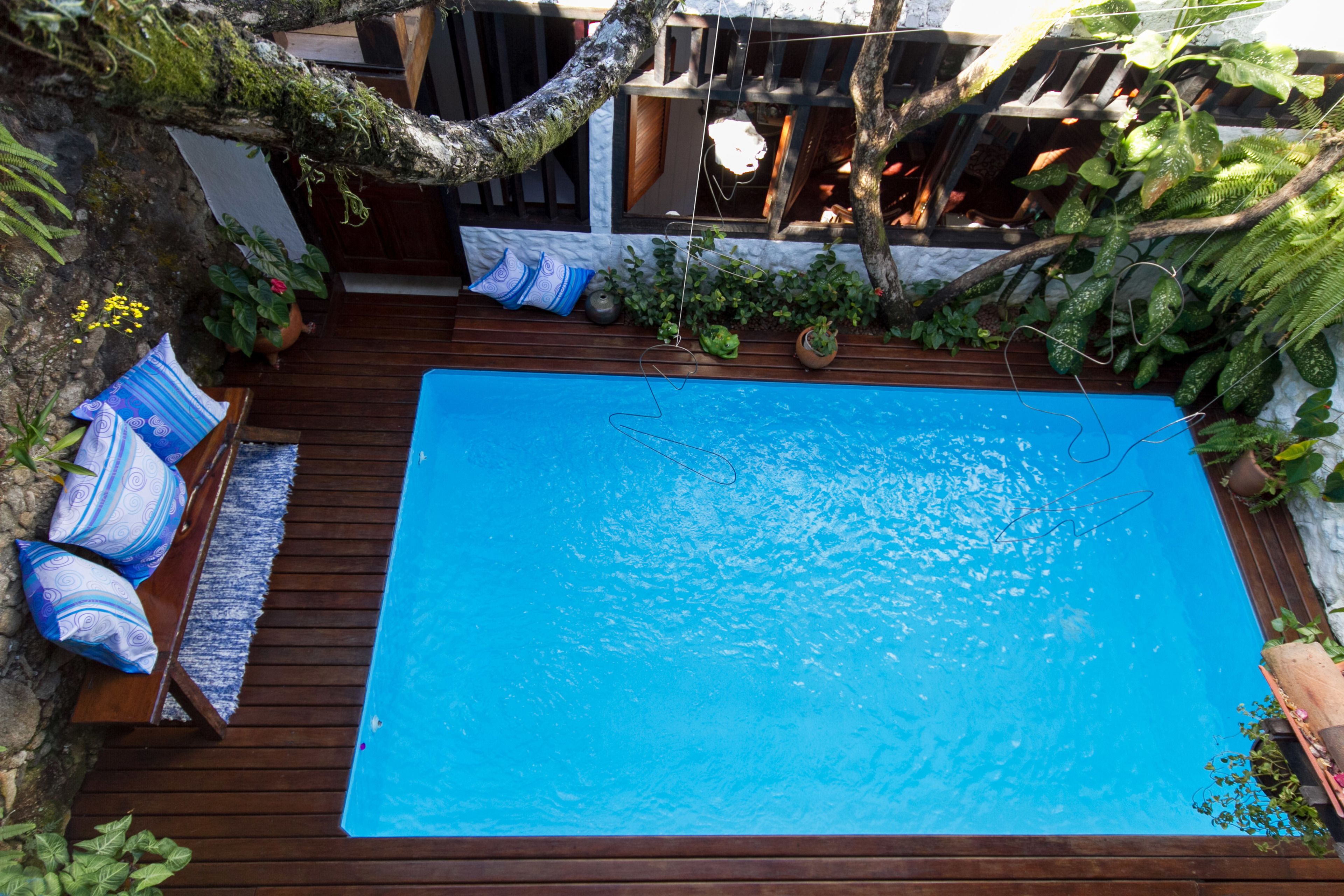A rectangular swimming pool with a wooden deck and blue cushions.