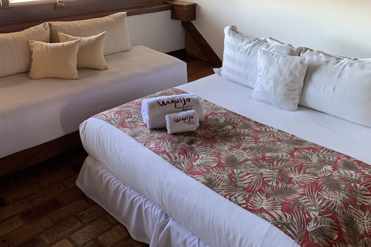 A bedroom with two beds, a wooden ceiling, and a window with curtains.