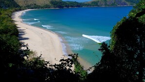 Una playa con aguas azul turquesa, orilla de arena y colinas verdes al fondo.
