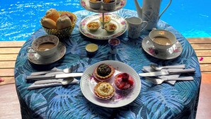 Mesa dispuesta con diversos alimentos y bebidas, incluyendo pasteles, sándwiches y un juego de té, junto a una piscina.