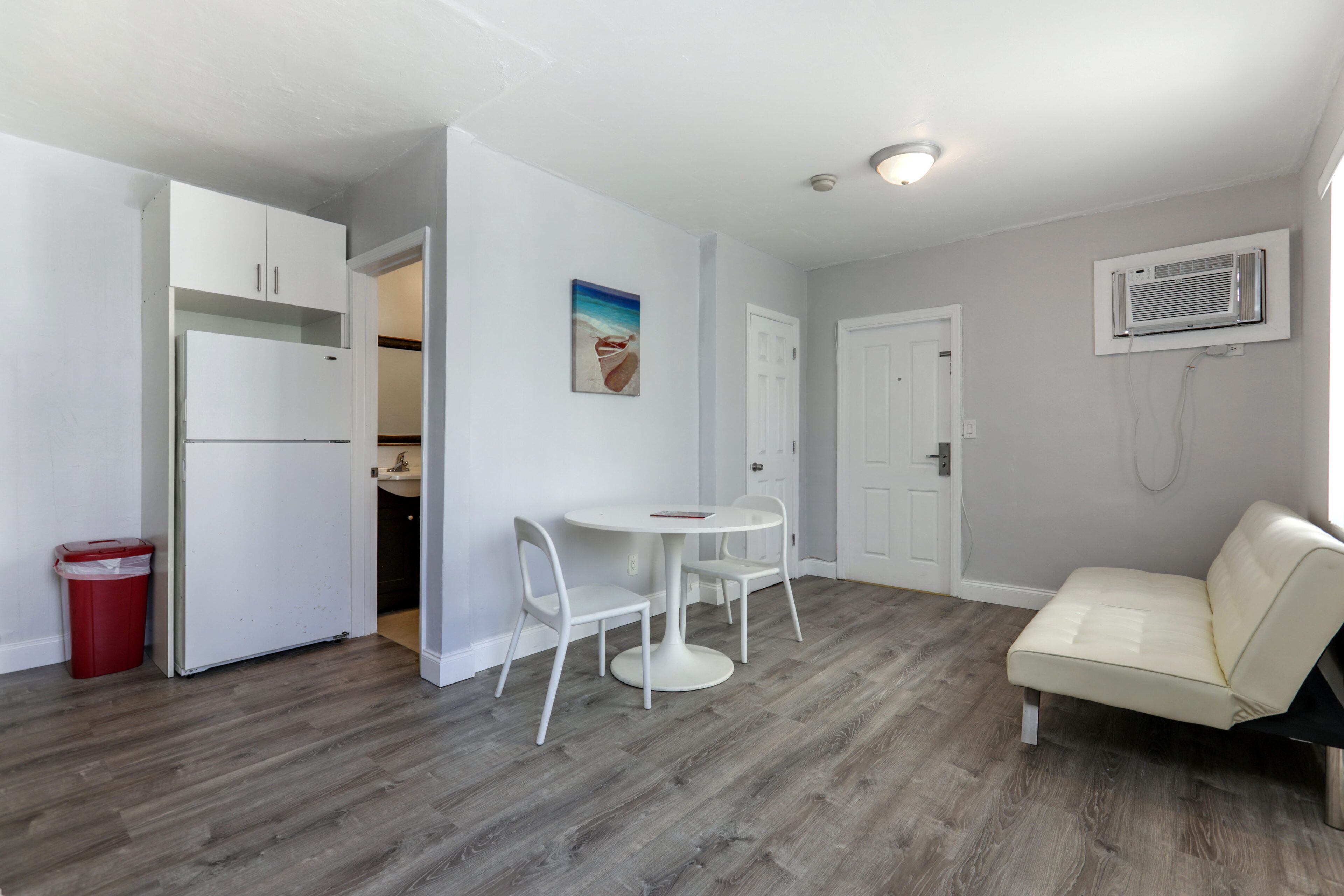 A compact living space with a kitchenette, a dining area with a table and chairs, a sofa, and a painting on the wall.