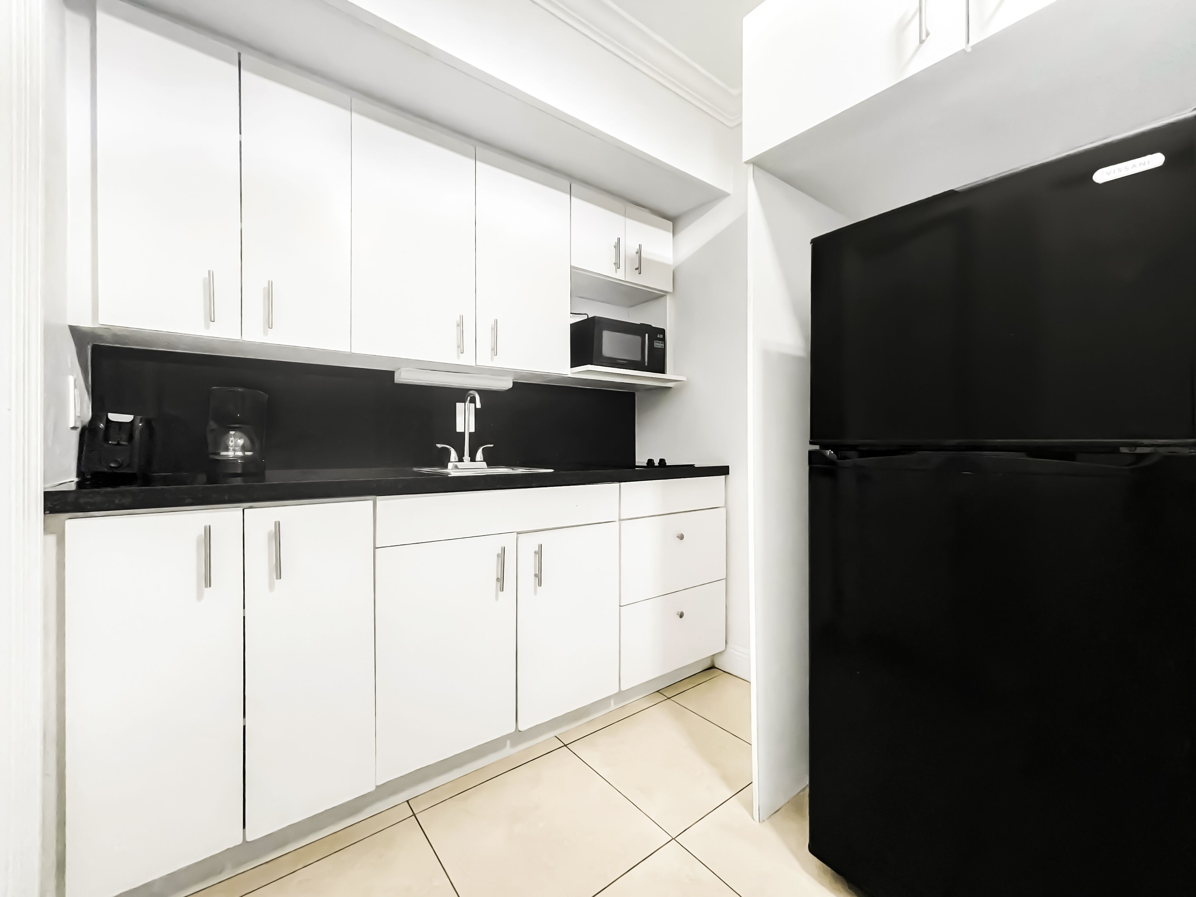 Eine moderne Küche mit weißen Schränken, einer schwarzen Arbeitsplatte und einem schwarzen Kühlschrank.