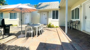 Un patio con una mesa, sillas, una parrilla y una sombrilla.