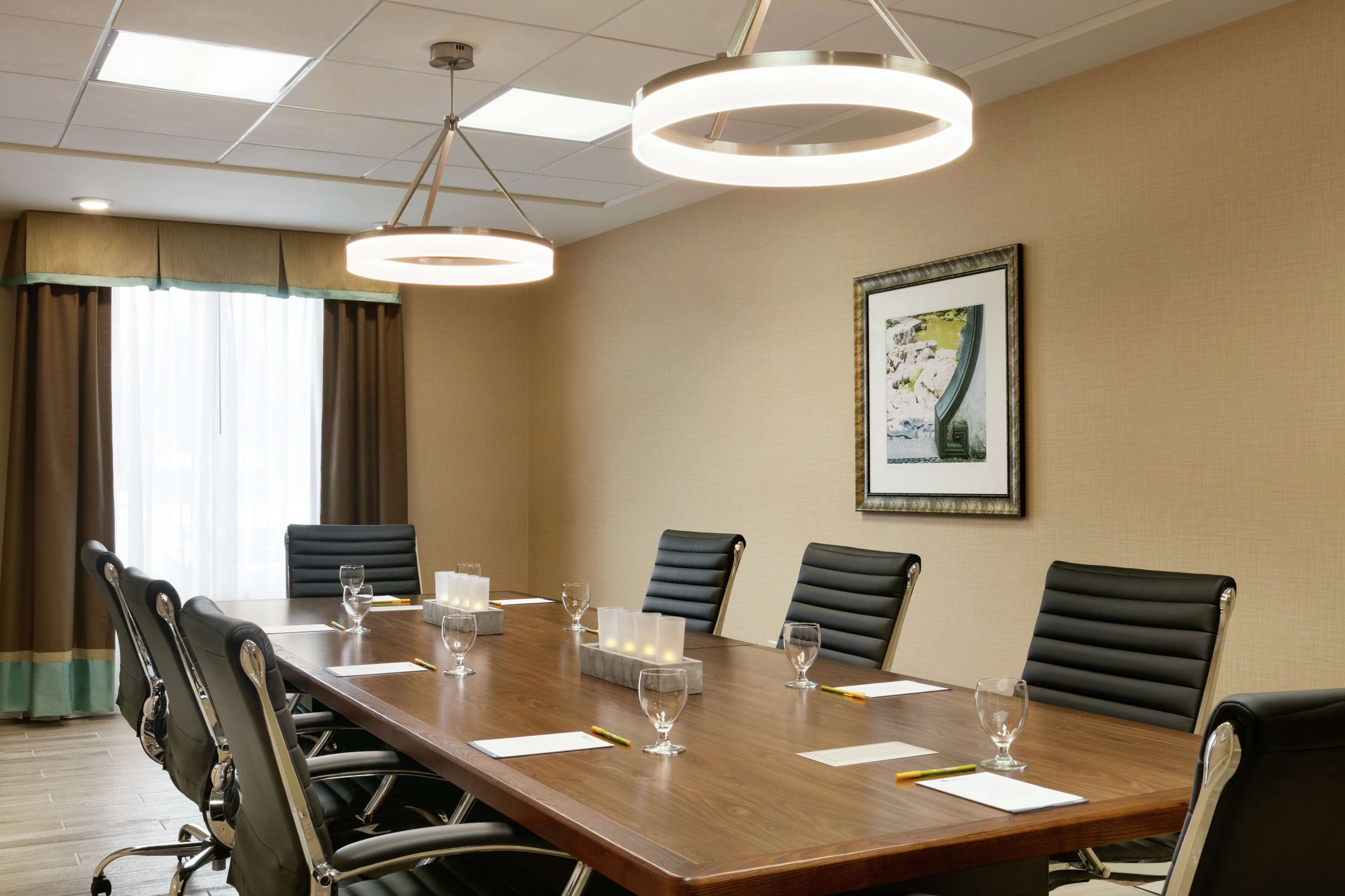 A conference room with a long wooden table, black leather chairs, and a framed picture on the wall.
