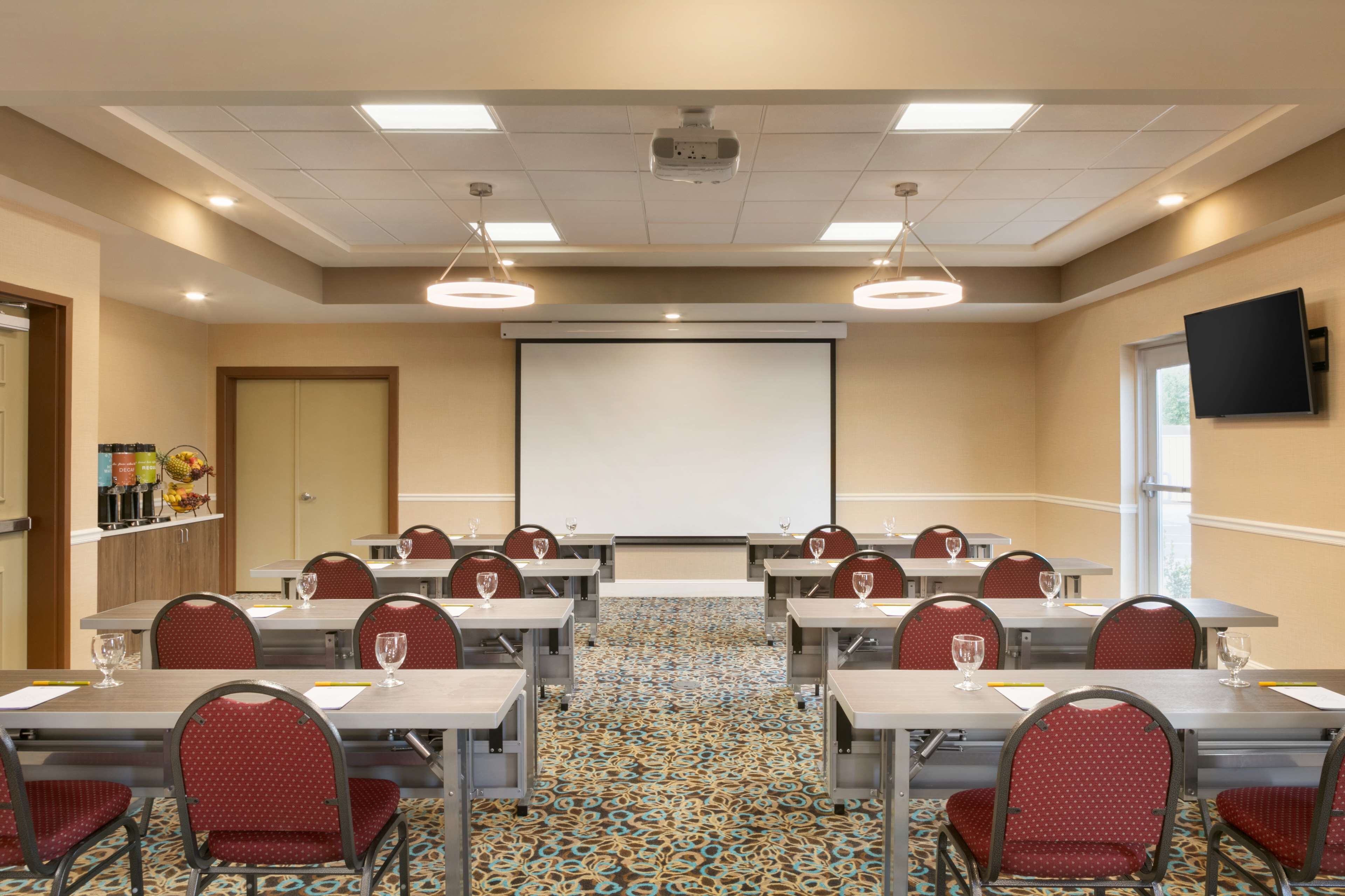 A conference room with tables, chairs, a projector screen, and a carpeted floor.