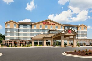Un Hilton Garden Inn con un diseño moderno, varios pisos y una entrada central con zona cubierta.