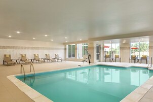 Una piscina interior con agua cristalina, rodeada de sillas de descanso y un suelo de baldosas.