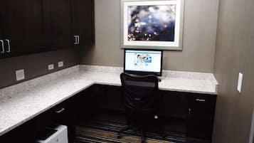 A small office space with a desk, chair, and a computer monitor. There is a framed picture on the wall and a carpeted floor.