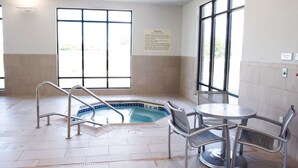 An indoor swimming pool with a hot tub, metal chairs, and a safety sign.