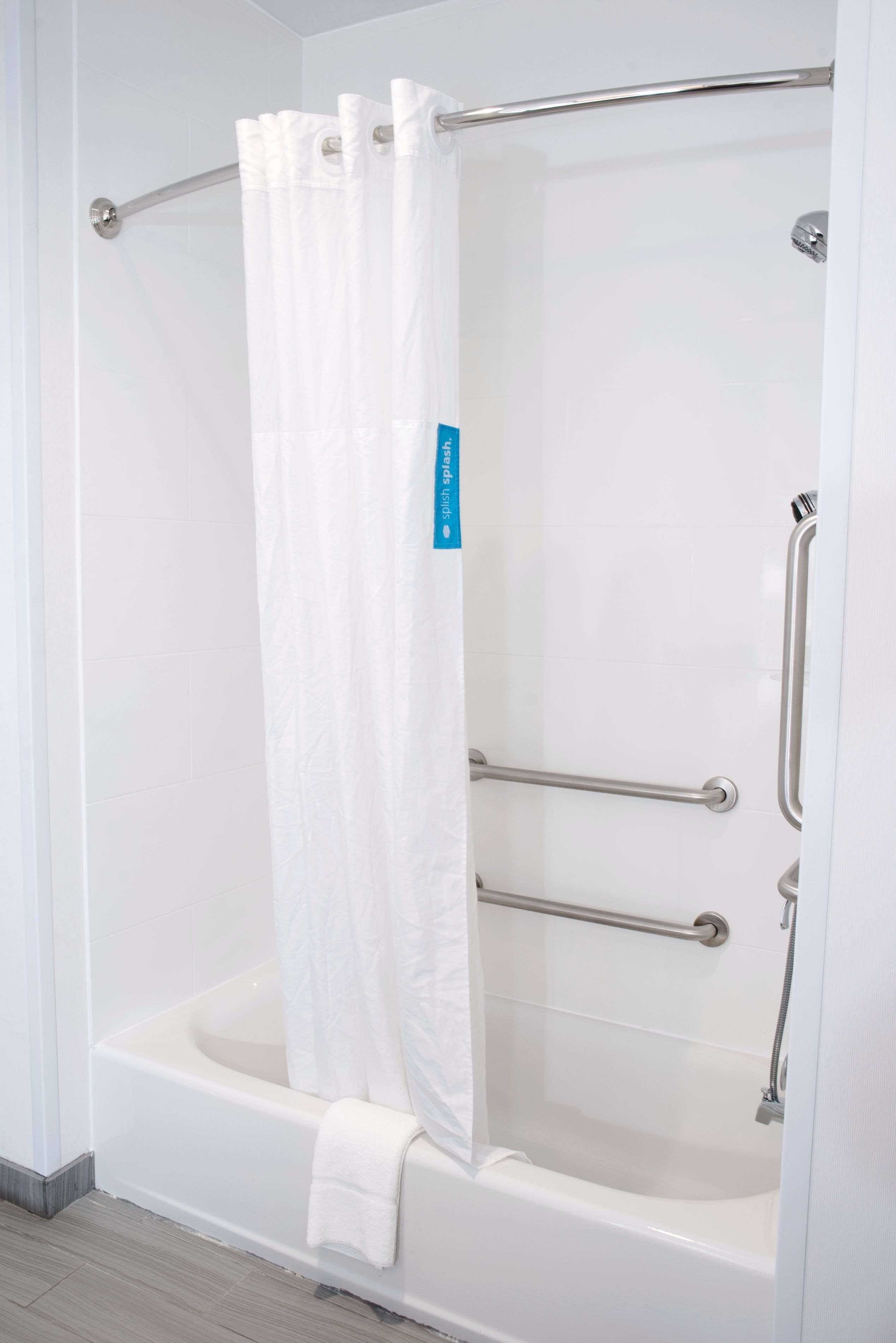 A white bathtub with a shower curtain and grab bars.